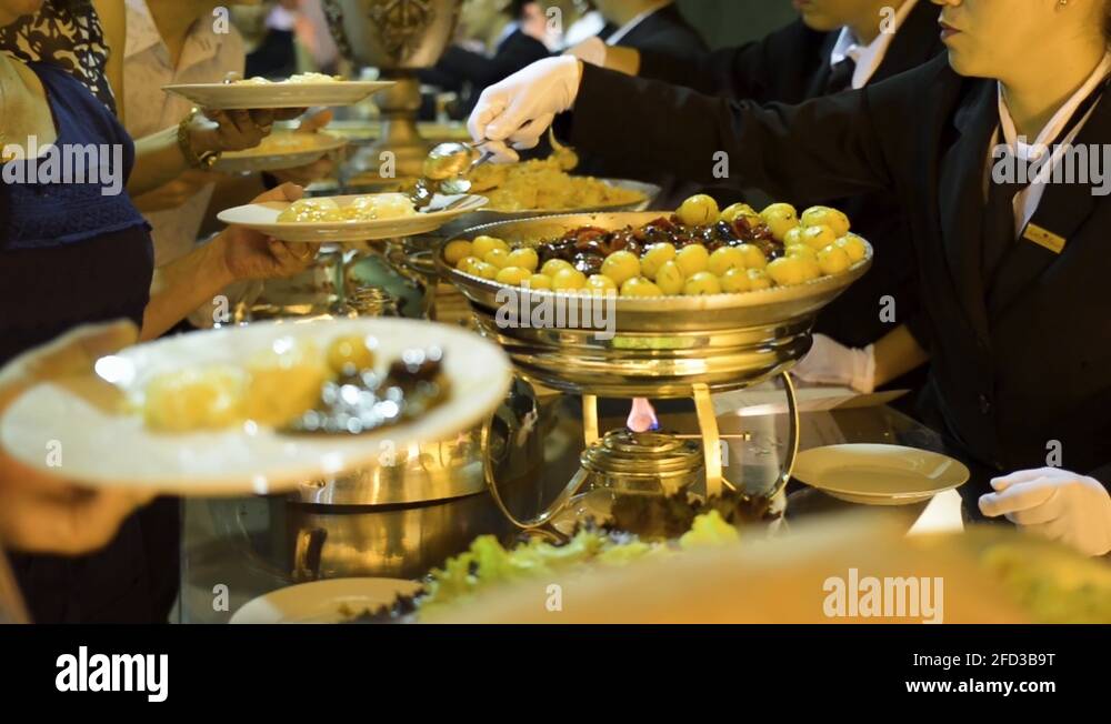 Waiters serving guests at a party buffet, the food table is plentiful