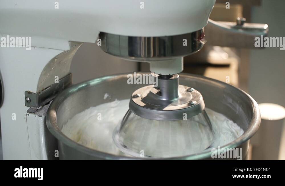 Whipping of cream in metal bowl with big electric mixer machine at the