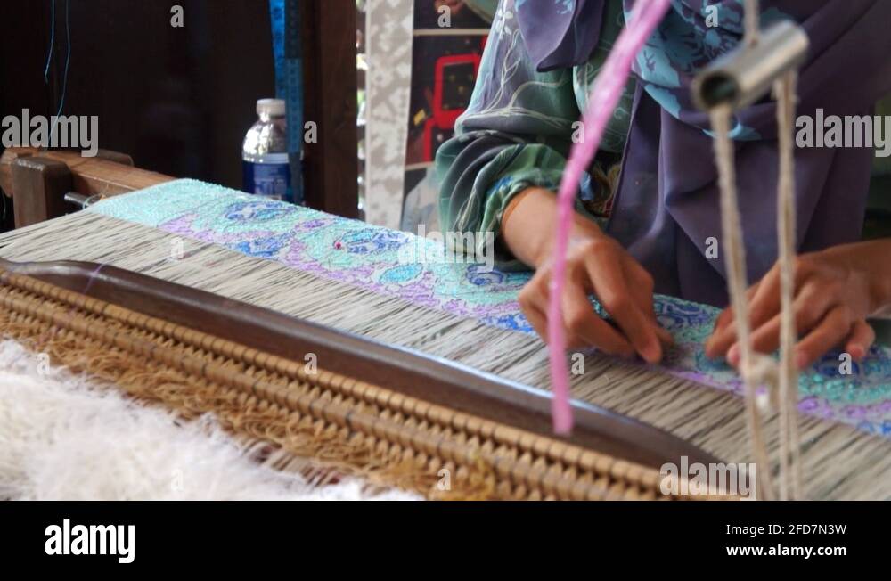 A woman is using traditional weaving machines to weave songket. Songket