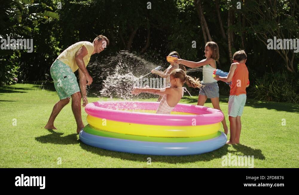 Father and children splashing water in inflatable pool in backyard