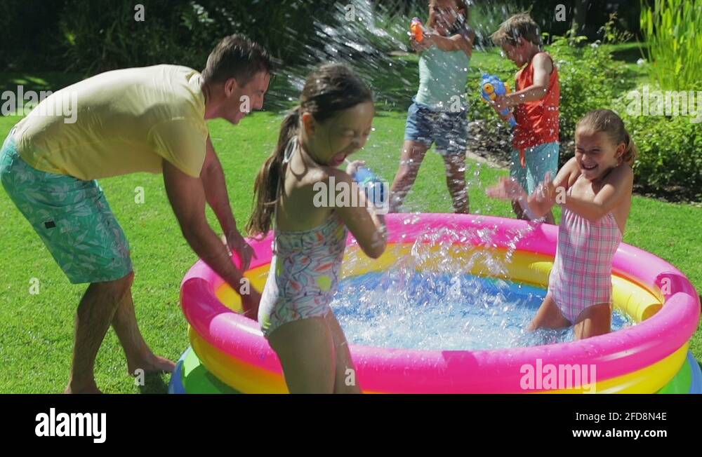 Family splashing water in inflatable pool in backyard Stock Video