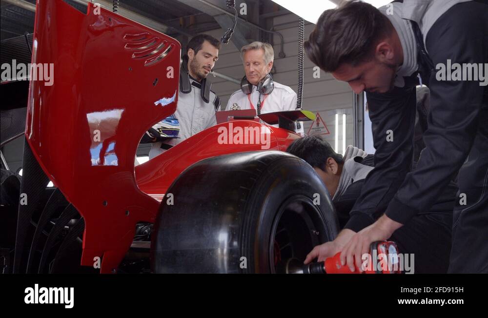 Race car manager and driver talking behind race car team working on