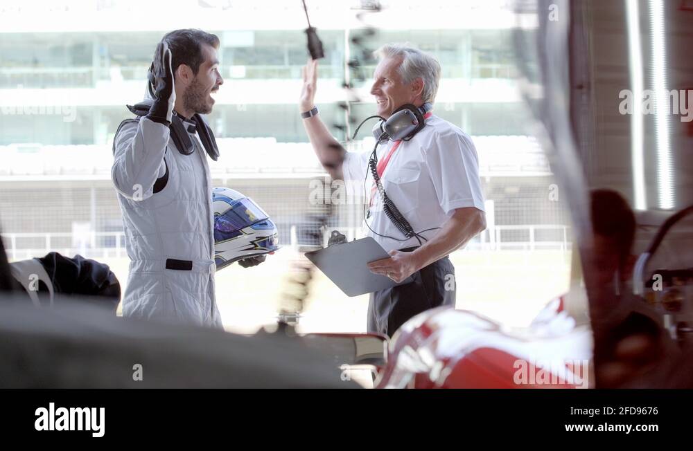 Race car manager and driver high fiving behind race car team working on