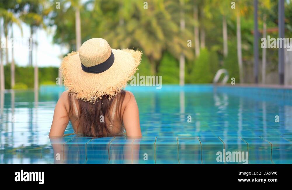 A woman wearing a straw hat, relaxing in an infinity pool at a luxury ...