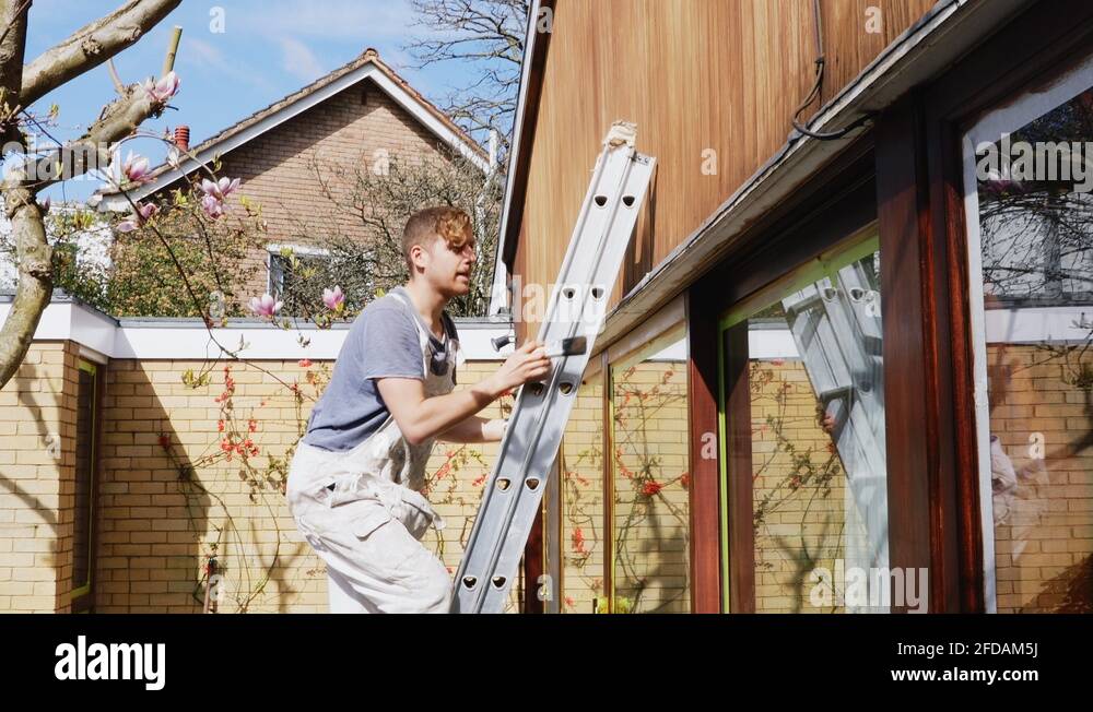 Male painter on ladder cleaning ledge, taping house exterior Stock