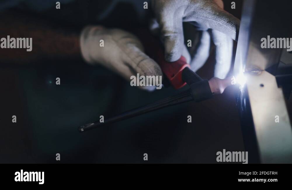 Tradesman wearing PPE, carefully TIG welding steel frame in dark