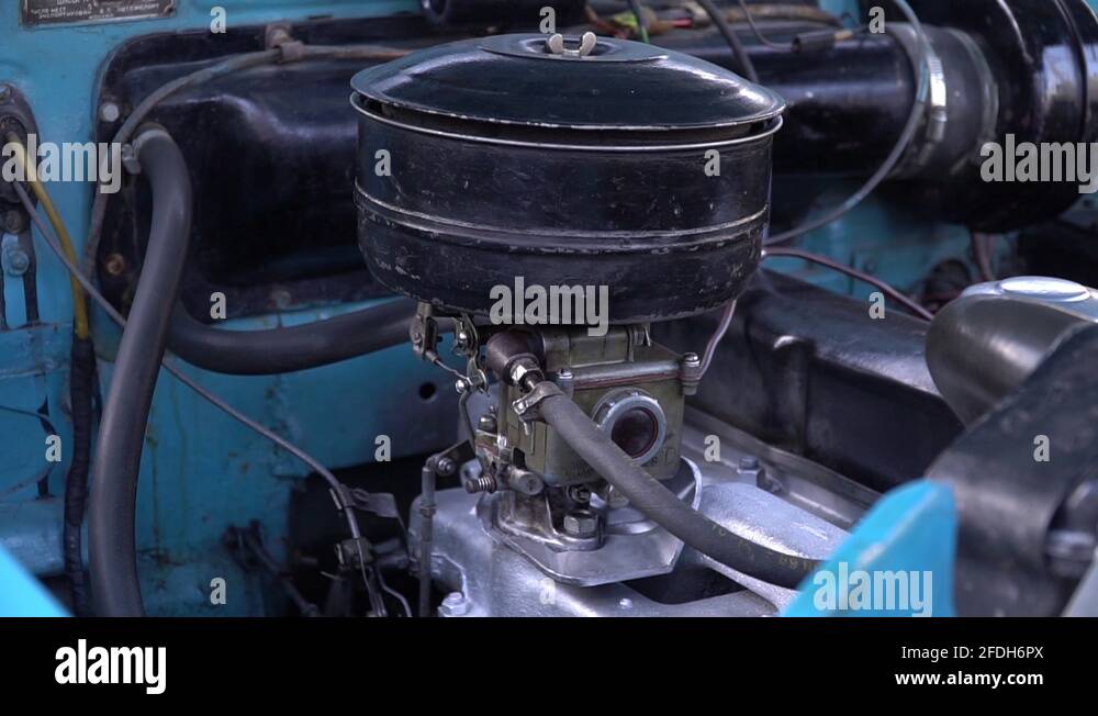 Old carburetor engine runs in retro blue car. View of the engine