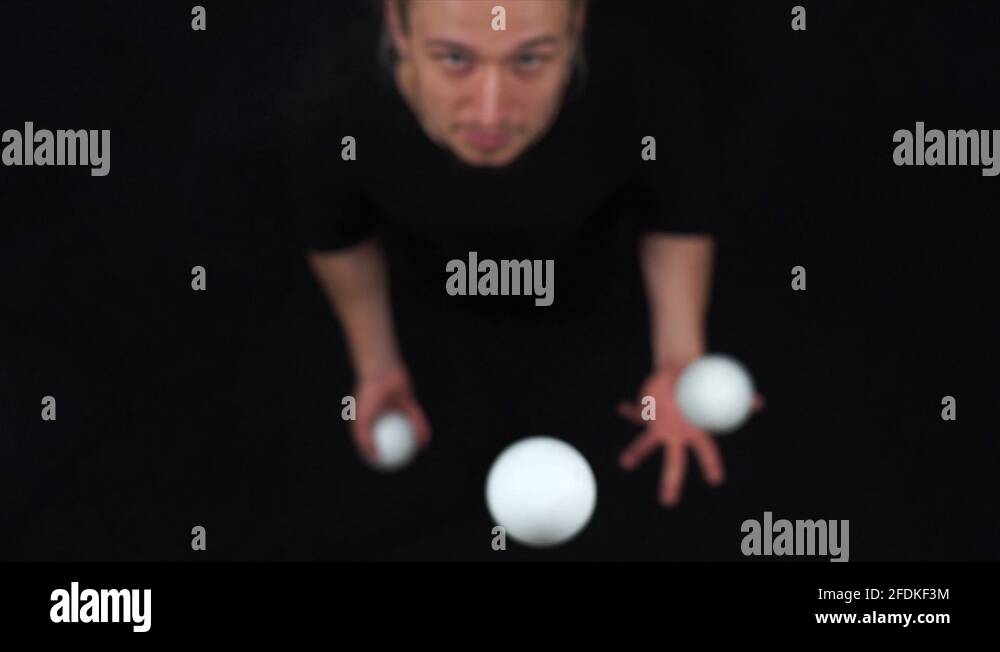 Circus artist wearing black juggling with white balls in slow motion