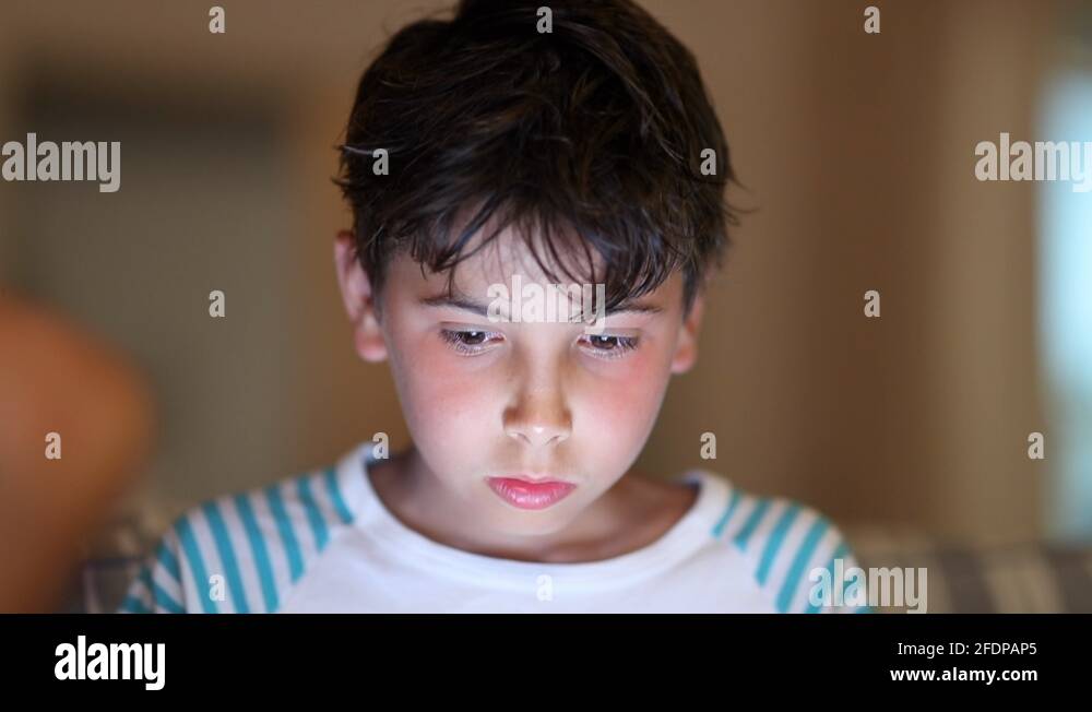 Boy using tablet screen at night. Child staring blue light device Stock