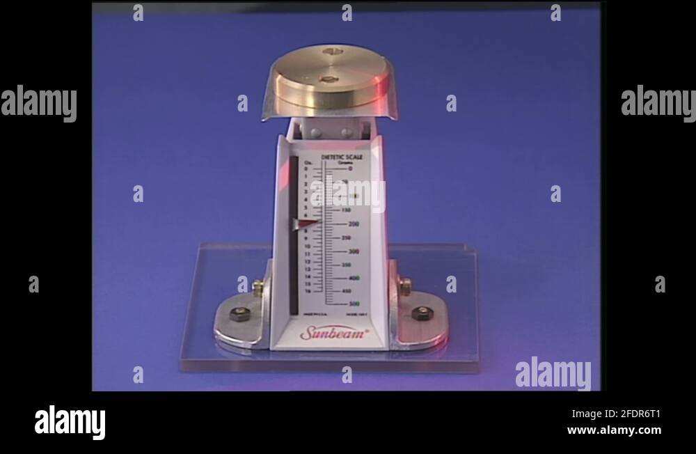 1990s Metal weight on Sunbeam scale. TV Studio, woman mounts scale on