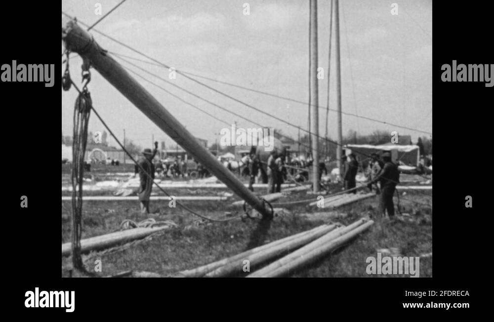 1940s Workers and elephants erect circus tent pole. Men hammer wooden