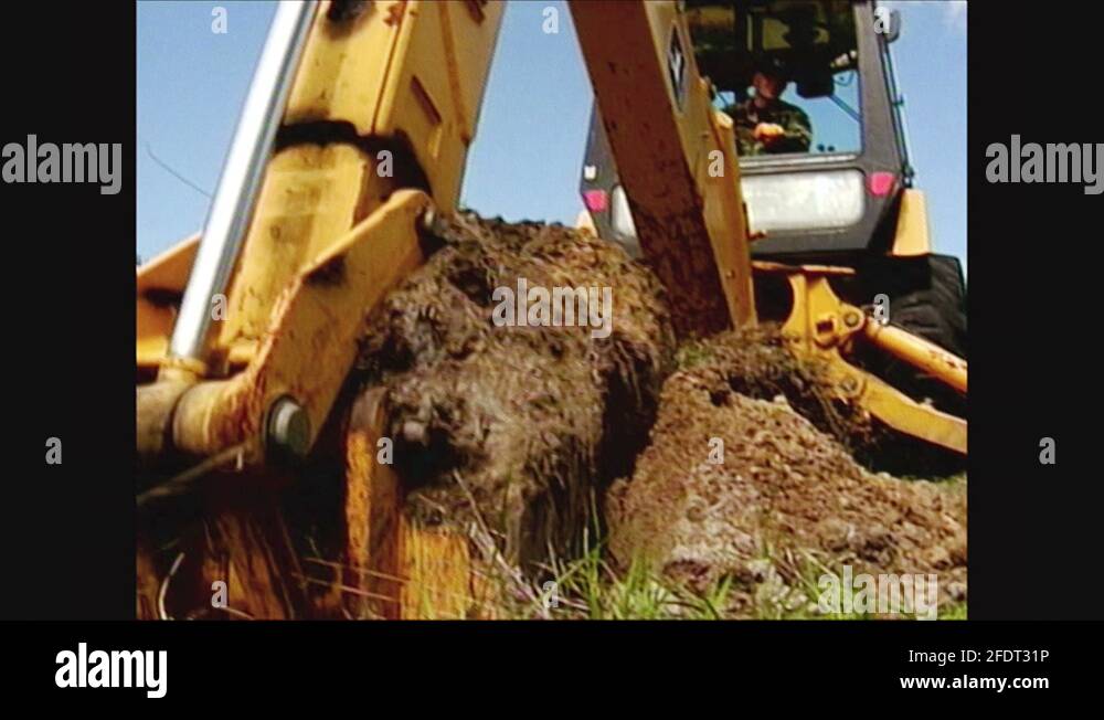 2000s Low angle, excavator bucket lifting dirt. Man operating