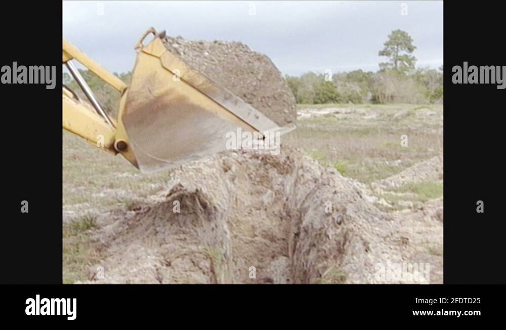 2000s Excavator bucket moves over ditch, drops dirt into ditch. Bucket