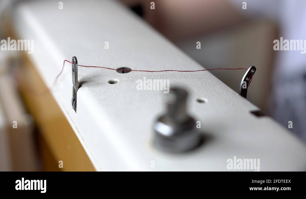 Thin red thread transporting over white sewing machine down to the