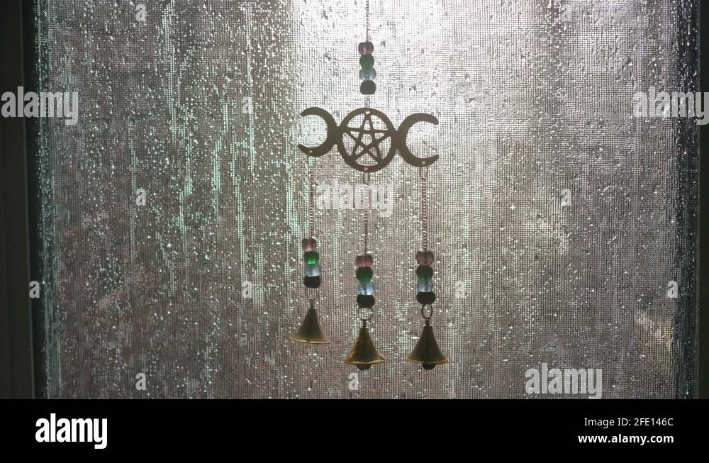 Static shot of a pentagram chime hanging in a screen window wet with