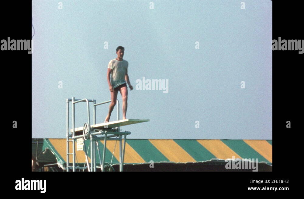 1960s Man jumps from high dive board at public pool and does a