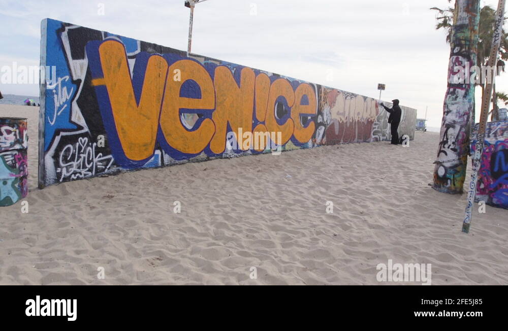 A man spray painting street art on a graffiti wall in Venice Beach in
