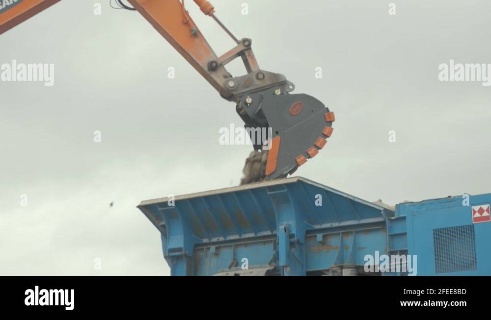 Digger bucket attachment tilting dropping stone into rock conveyor in
