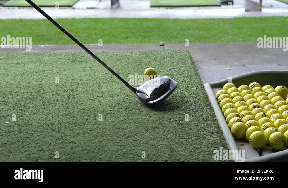 tray of balls and person hitting with a golf driver off the mat Stock