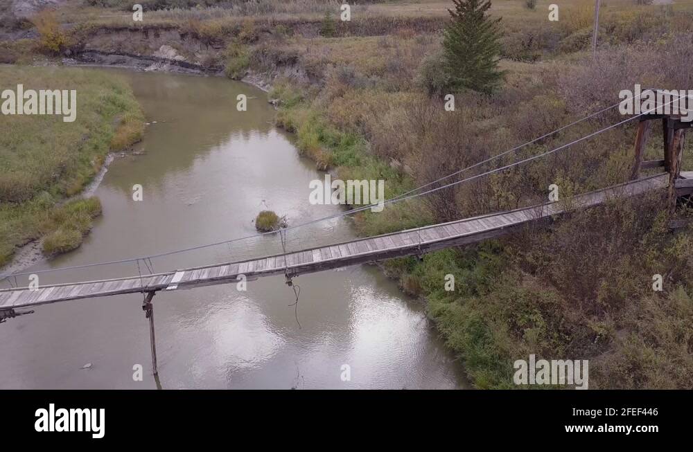 Battered and neglected old suspension bridge over tiny badlands river ...