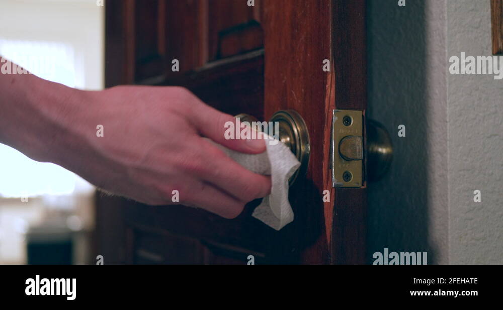A hand cleaning and sanitizing a door knob covered in germs and virus