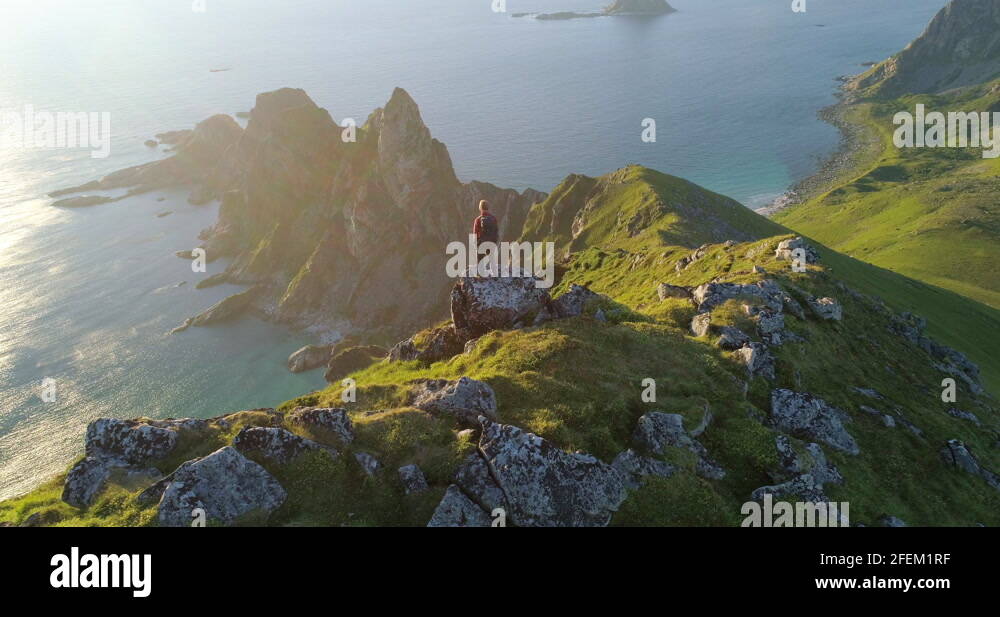 Pointed Ridge Norwegian hiker on arctic mountain in midnight sun looking at pointed ...