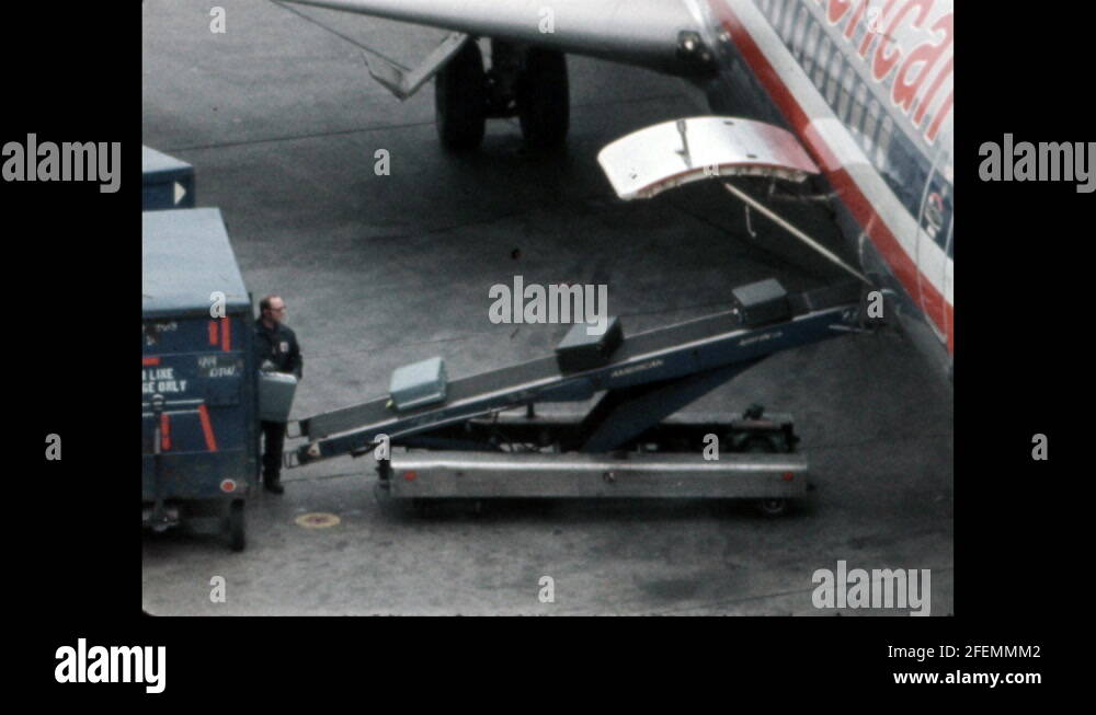 1960s Luggage is loaded onto conveyor belt up to airplane. Airplane in