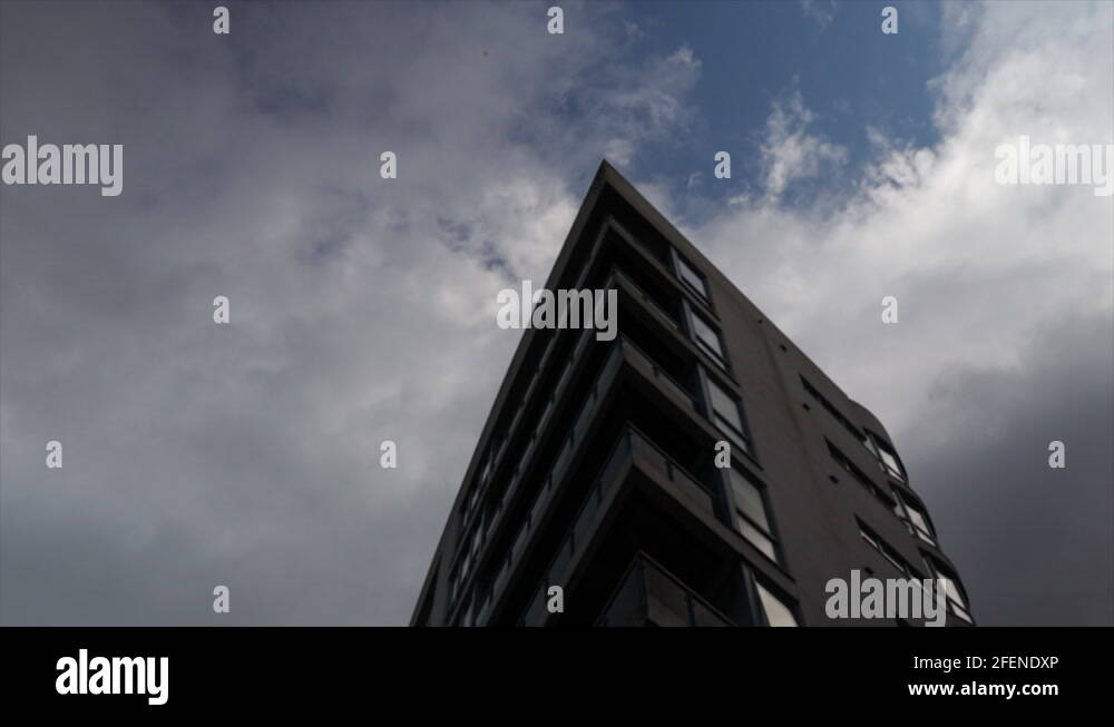 Cloudy blue sky tilting down to reveal modern apartment building at point Stock Video Footage