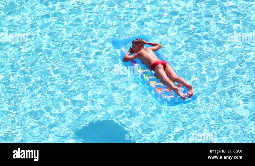 Boy floats in pool lying on stomach at inflatable mattress Stock Video