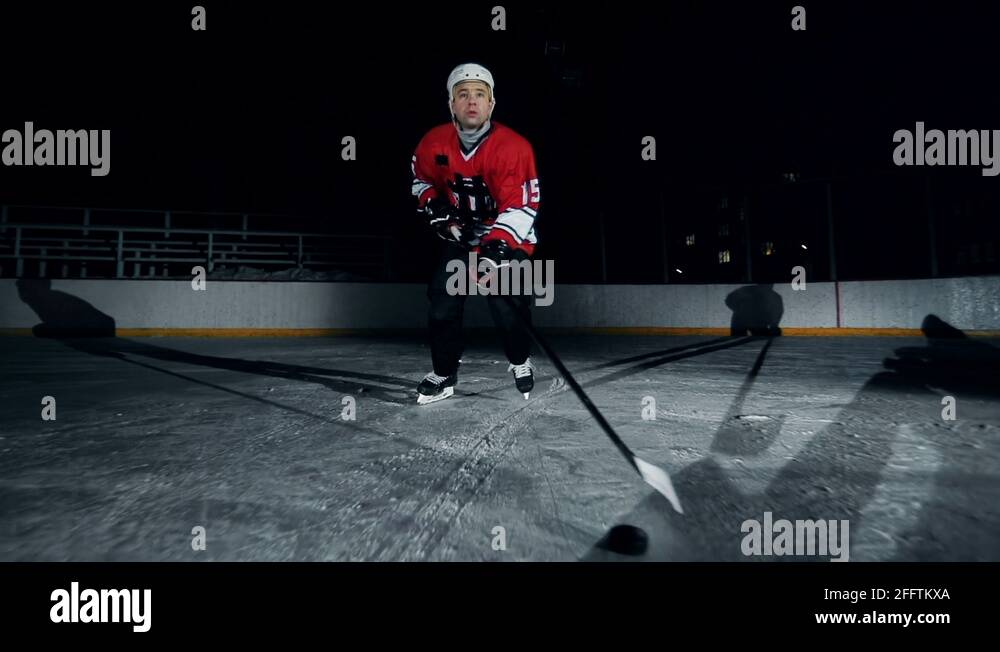 Hockey player ice skating with lshaped hockey stick pushing puck Stock