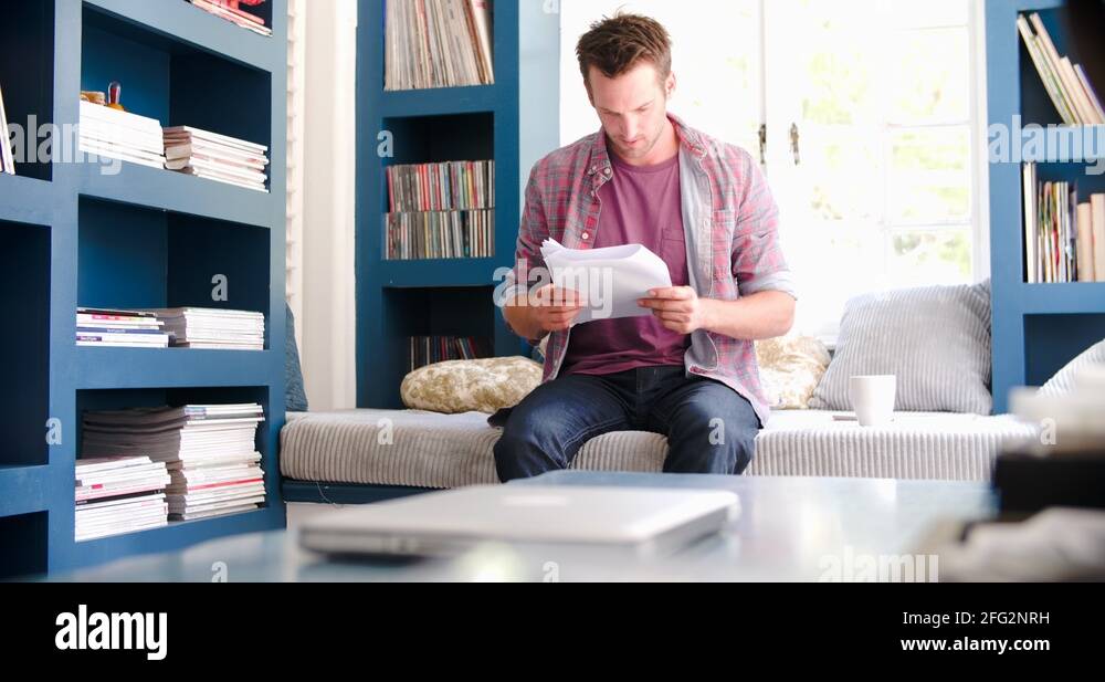 Worried Man Sitting On Couch In Home Office Reading Document Stock