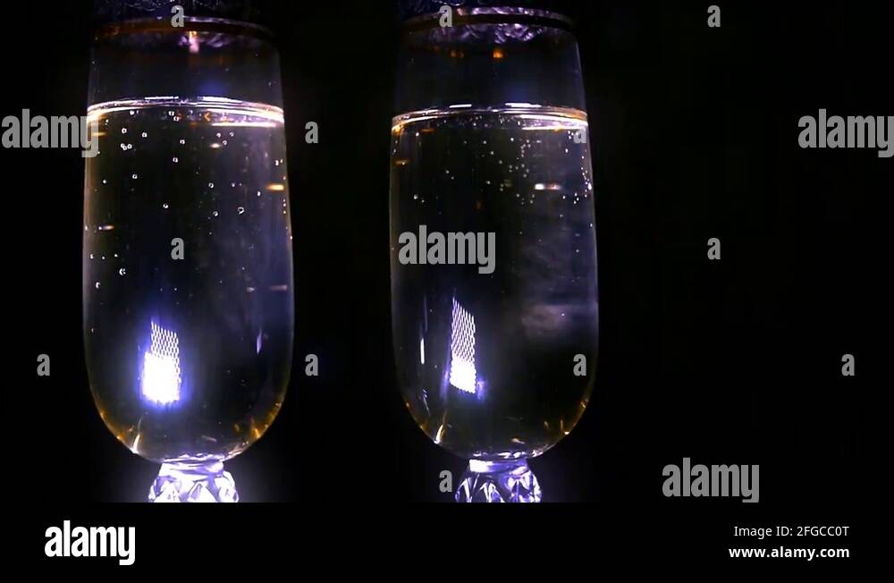 Bubbling champagne being poured into two crystal glasses against black