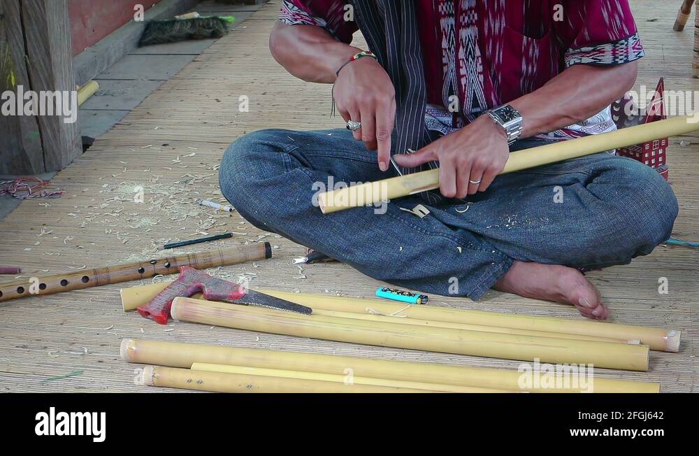 Balinese craftsman hand carves flutes from bamboo tubes in Indonesia