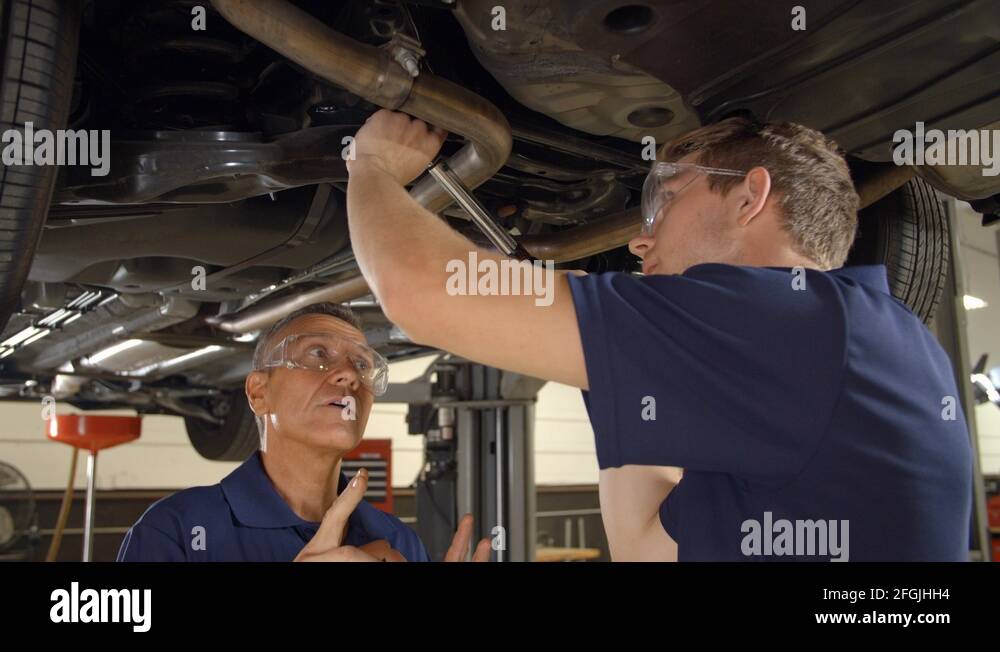Mechanic And Male Trainee Working Underneath Car Together Stock Video