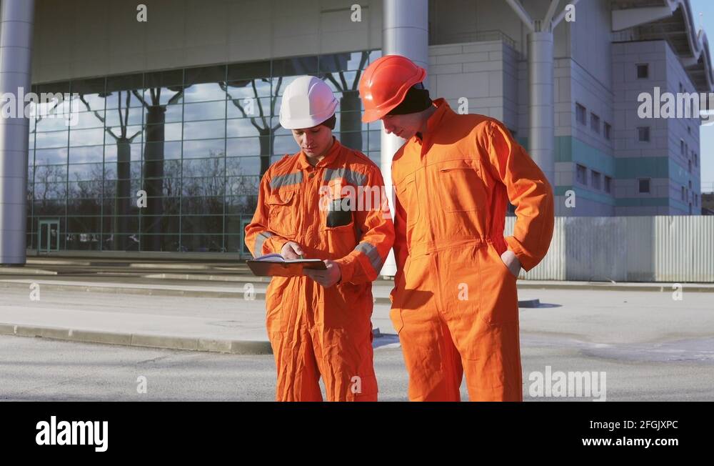 Two construction workers in orange uniform and helmets looking over ...