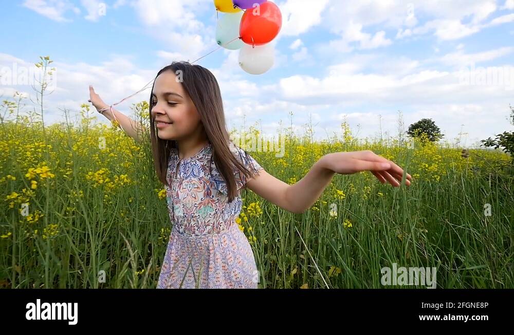 little girl in a dress running through yellow wheat field with balloons ...