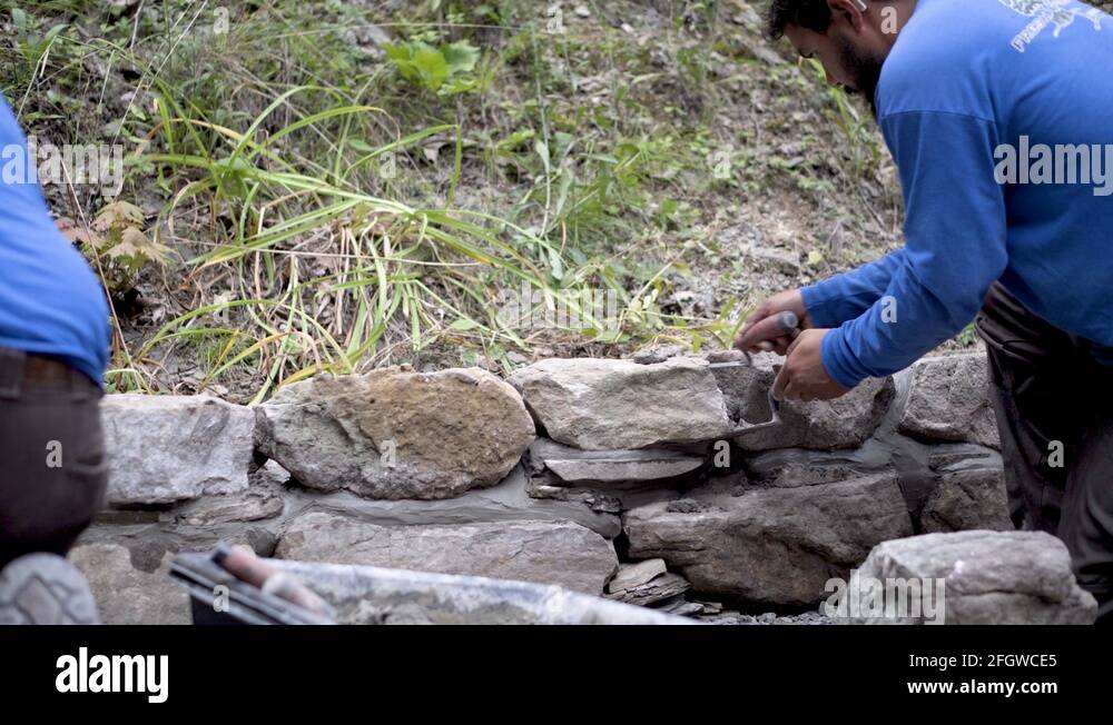 Putting Rocks On Rocks Hardscaper putting mortar between rocks in a stone wall with two ...