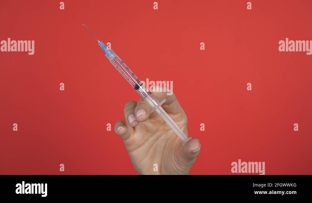 Female hand holds up medical syringe hypodermic needle. Drop at tip