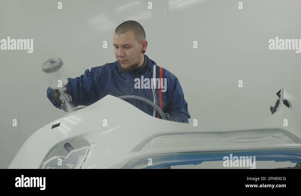 Auto painter spraying white paint on car front bumper in special booth