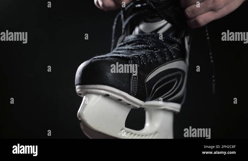 A player in hockey, ties laces on skates, a black background. Close up