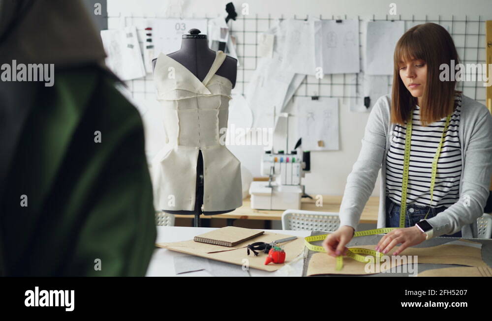Attractive female tailor is measuring clothing patterns with tape