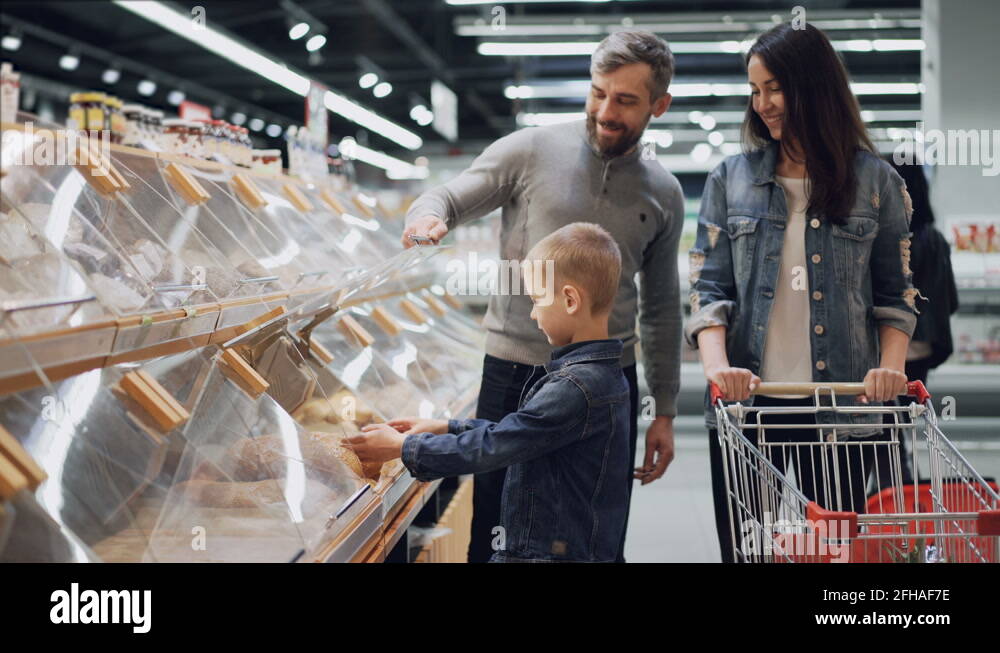 Adorable little boy is helping his parents to choose bread in bakery