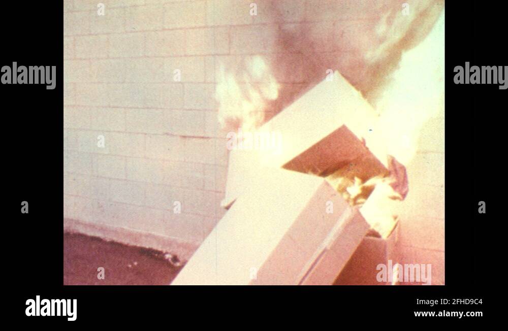 1970s Man uses liquid fire extinguisher on burning cardboard. Man at