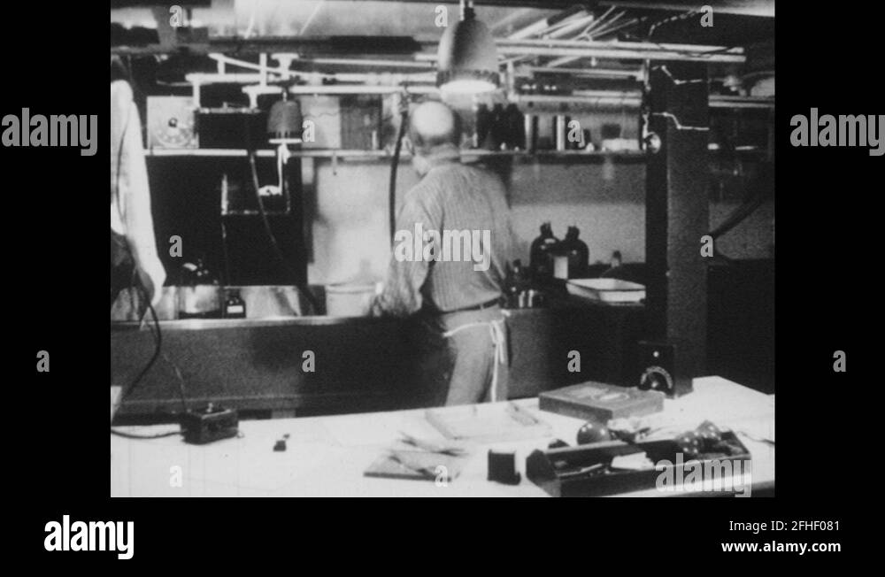 1950s Man works in darkroom photography studio, uses chemicals, dries