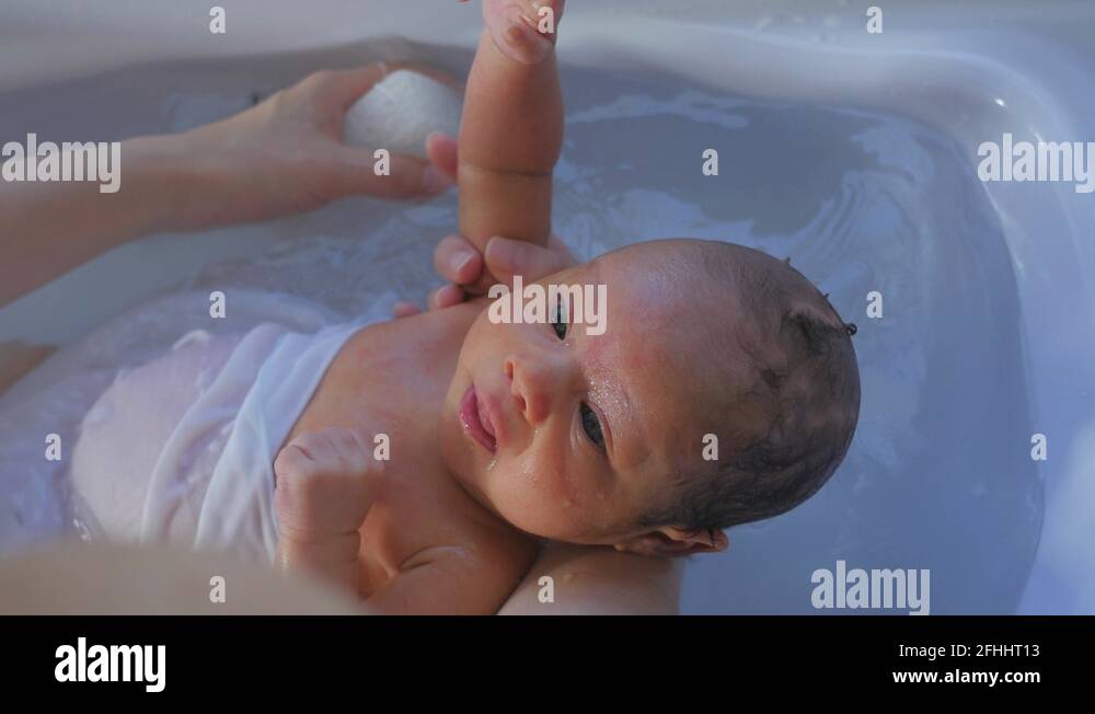 Newborn baby bathed by mother in tub. Squeezing water from sponge on