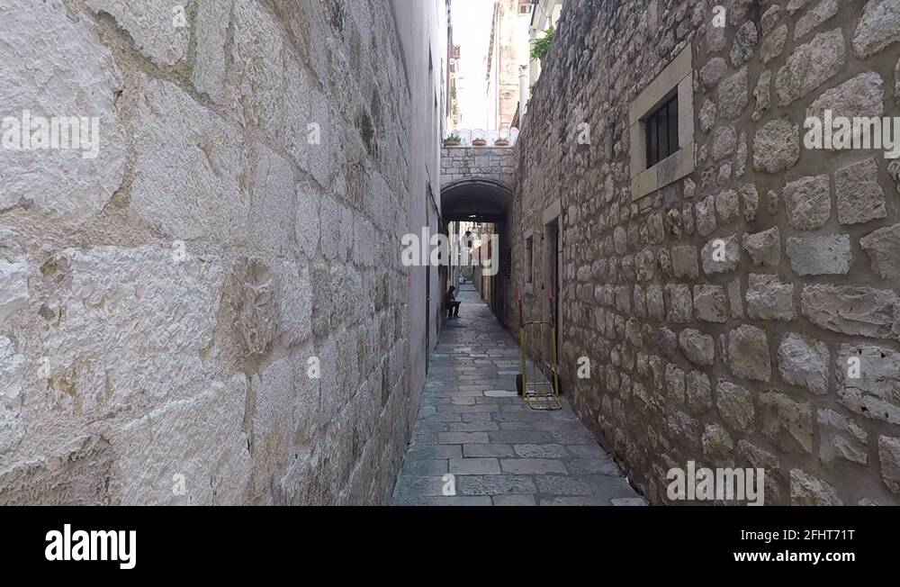 A man sitting on a long narrow stone street, locked off camera Stock
