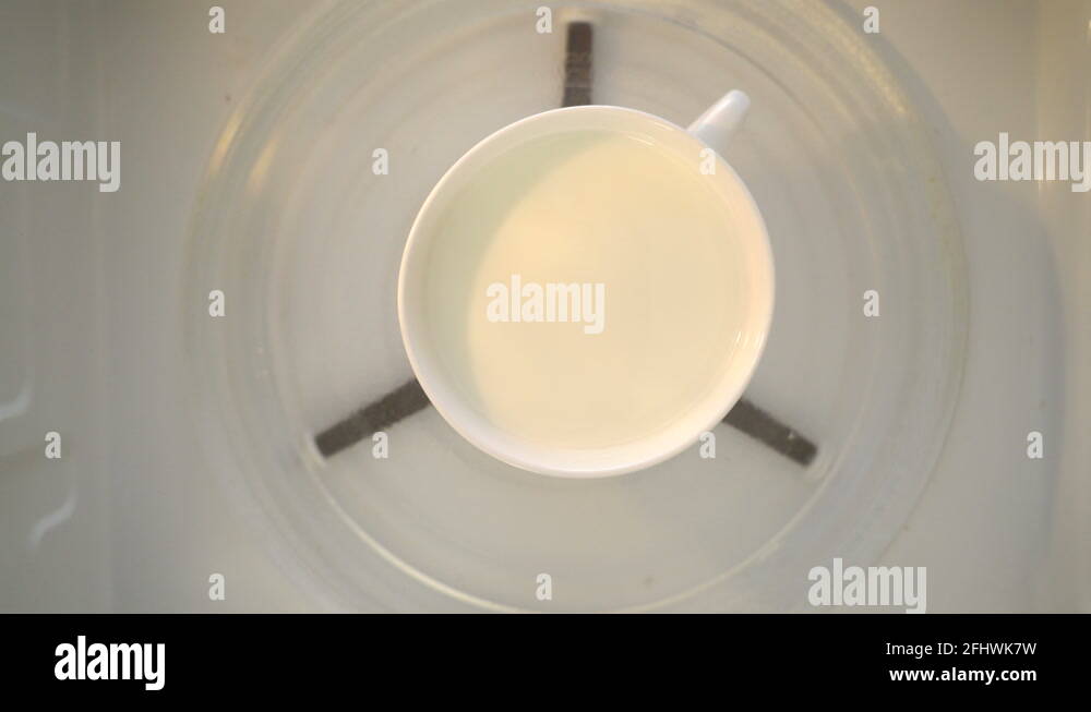 Heating milk in microwave. Mug of milk turning around in microwave top