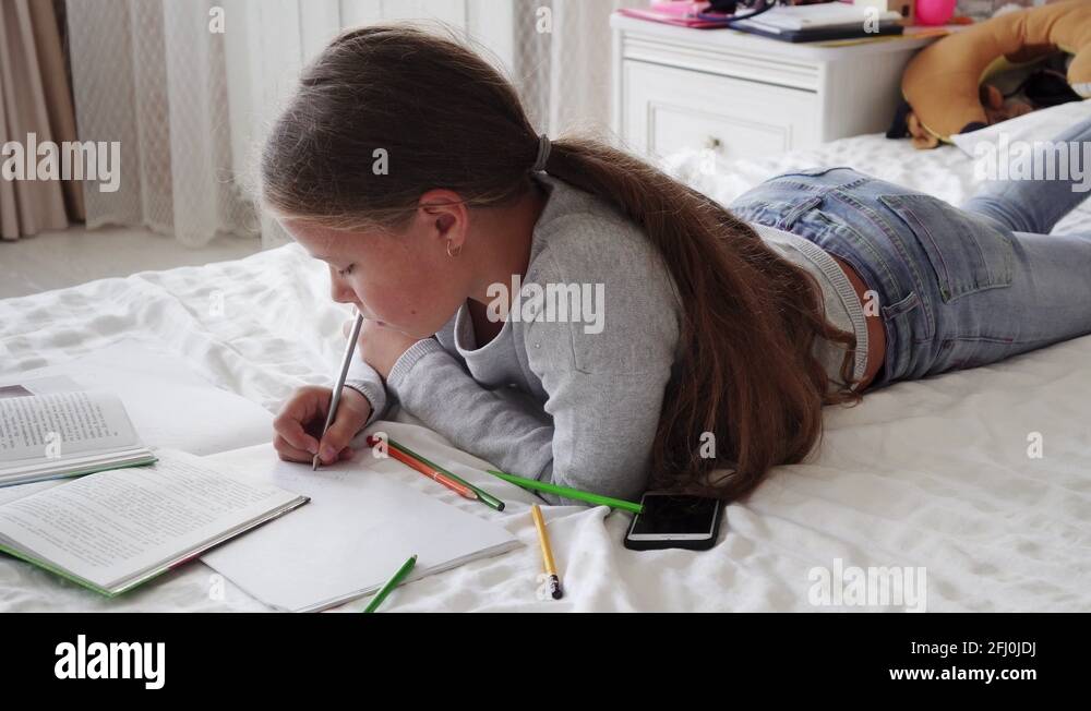 Little school girl lying on bed and doing homework Stock Video Footage