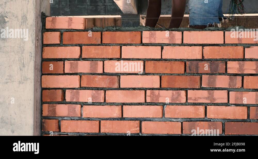 Asian man laying bricks on top of mortar to build brick wall Stock