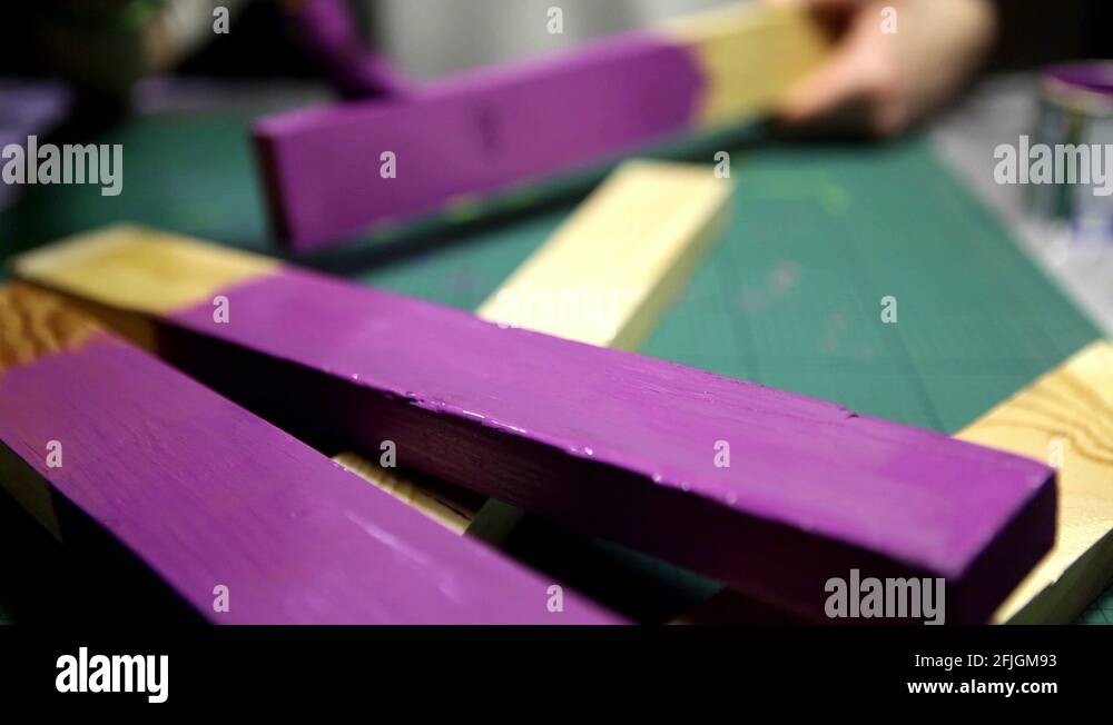 Focus change to a girl painting a wood stick with purple varnish in the